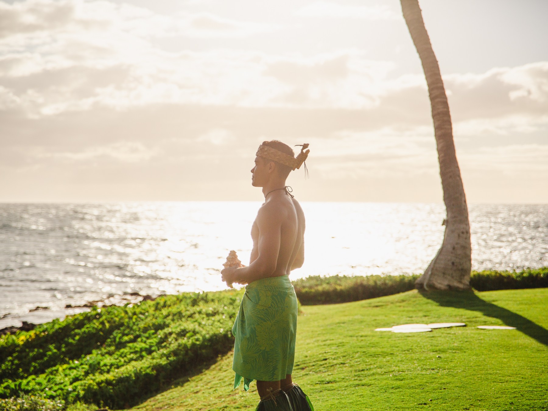 Kauai Man in Luau Attire holding Conch Shell Looking Out Over the Ocean