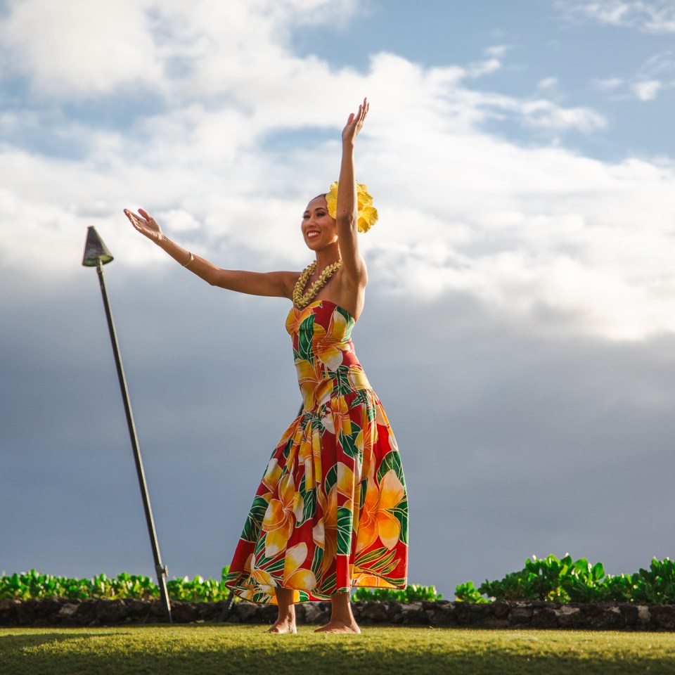 Women in Dress with flower in her hair raising her arms to the sky during a Kauai Luau Dance Women in Dress with flower in her hair raising her arms to the sky during a Kauai Luau Dance