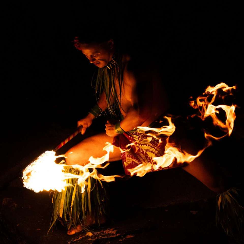 Performer in traditional attire spinning fire at night.